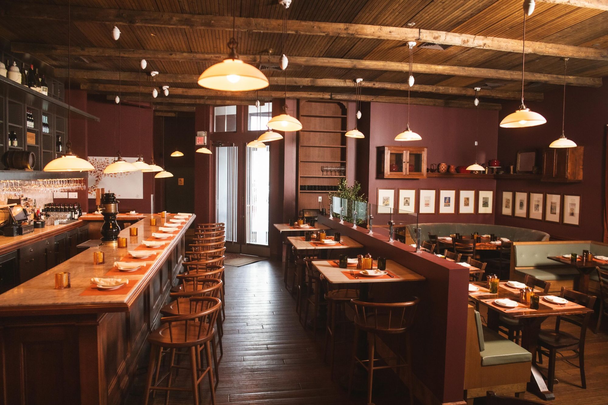 The dining room: a marble bar with wooden stools, tables under pendant lamps, and a beamed ceiling.